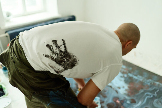 Caucasian young adult artist bending over canvas, creating contemporary floor painting in studio. Useful for creative business, art marketing, workshop promotion