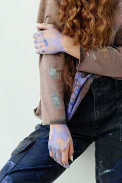 Vertical shot of young adult woman resting with paint covered hands and clothes, embodying contemporary artist workflow and creative process. Ideal for art branding, studio promotion, maker campaigns
