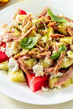 Close up of watermelon salad with feta cheese, canned tuna in olive oil and cucumbers on a set dining table