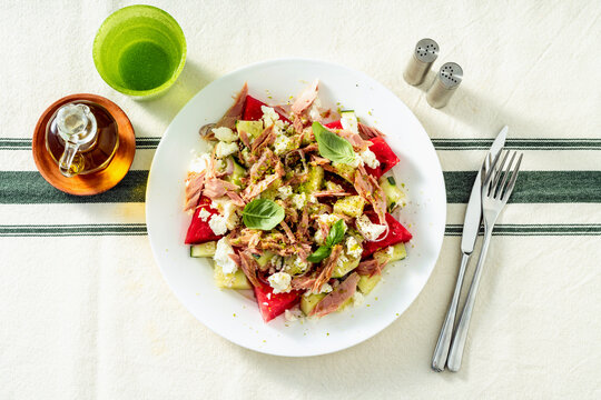Watermelon salad with feta cheese, canned tuna in olive oil and cucumbers served on a set dining table