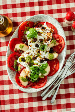Italian style salad with tomatoes, peaches, olives, burrata and pesto on a set dining table