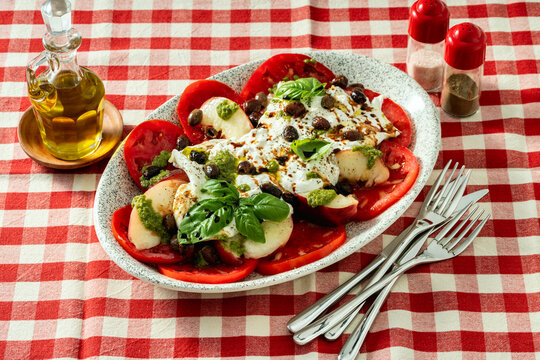 Italian style salad with tomatoes, peaches, olives, burrata and pesto on a set dining table