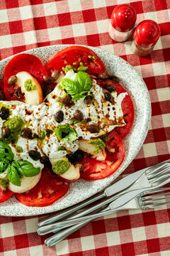 Close up of Italian style salad with tomatoes, peaches, olives, burrata and pesto on a set dining table