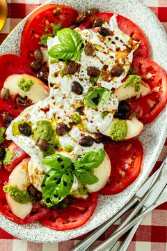 Close up of Italian style salad with tomatoes, peaches, olives, burrata and pesto on a set dining table