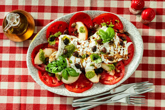 Italian style salad with tomatoes, peaches, olives, burrata and pesto on a set dining table