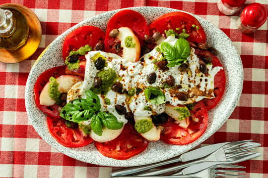 Close up of Italian style salad with tomatoes, peaches, olives, burrata and pesto on a set dining table
