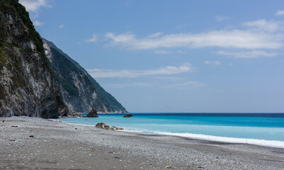 Fototapeta premium Qingshui Cliff in Hualien, Taiwan. Steep rocky cliffs overlook the turquoise Pacific Ocean. A grey pebble beach borders the water. Clear blue sky above.
