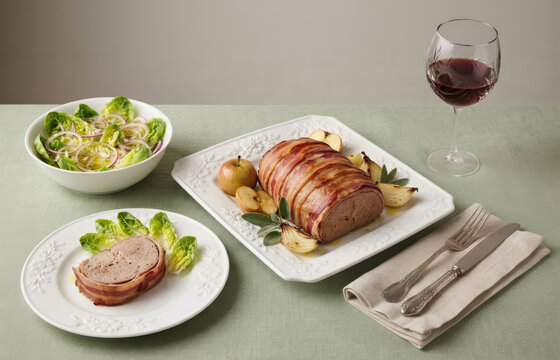 Delicious bacon-wrapped meatloaf roasted with apples, served with a fresh lettuce salad and a glass of red wine.