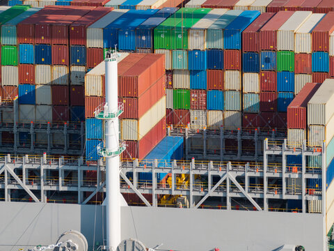 Aerial view of a cargo ship deck stacked with colorful shipping containers and a white mast in the United Kingdom.