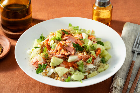 Baked salmon salad with cucumbers, chickpeas, walnuts, feta and rice served on a summer style dining table