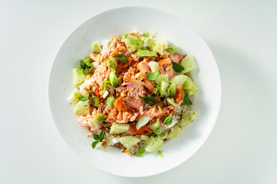 Baked salmon salad with cucumbers, chickpeas, walnuts, feta and rice on white background