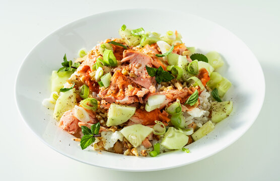 Baked salmon salad with cucumbers, chickpeas, walnuts, feta and rice on white background