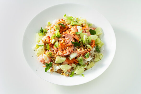 Baked salmon salad with cucumbers, chickpeas, walnuts, feta and rice on white background