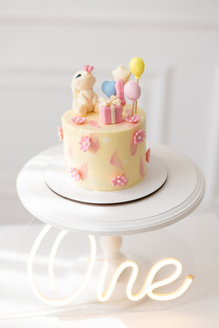 First Birthday Cake Decorated With Fondant Bunny Gift Box Balloons And Flowers On White Cake Stand