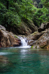 Sanzhanxi River waterfall in Taroko. Turquoise pool surrounded by rocky cliffs. Lush green forest covering canyon walls. Small cascade flowing into clear water. © Eugene Ga