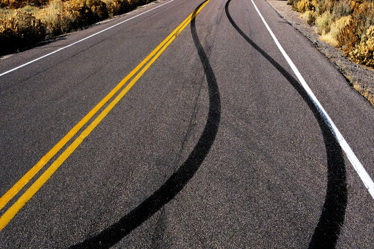 Dark Skid Marks on Asphalt of Road Crossing Yellow Traffic Lines from a Reckless Driver Driving Dangerously