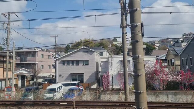 View from a moving train window showing a row of modern suburban houses in a typical Japanese residential neighborhood during the day.