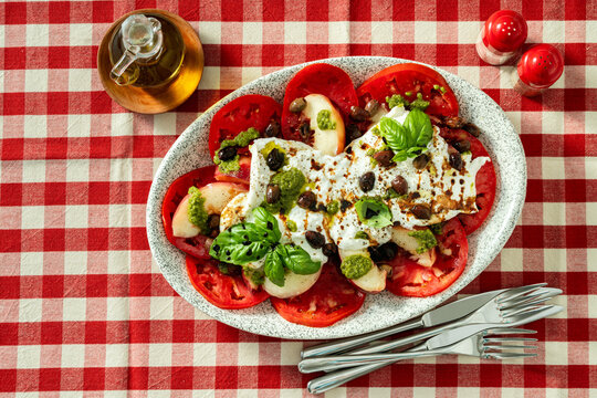 Italian style salad with tomatoes, peaches, olives, burrata and pesto on a set dining table