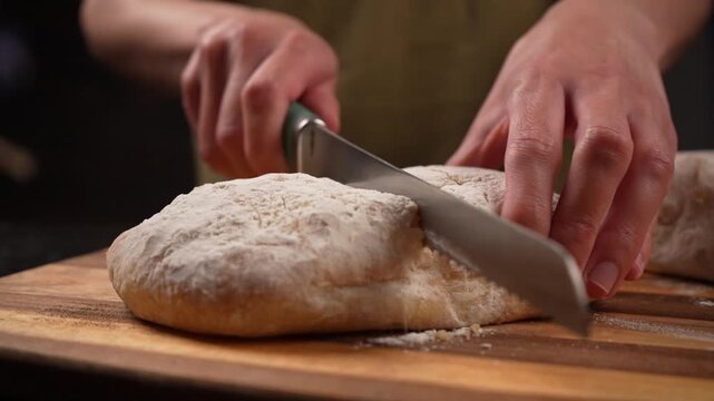 Soft, fresh yeast bread is being sliced ​​with a bread knife on a wooden table. slow motion