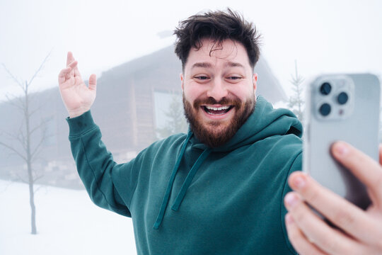Smiling man talking on smartphone outside snowy mountain cabin