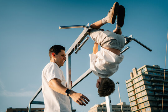 Man Teaches Boy to Do Pull-Ups in City Park During Sunny Day