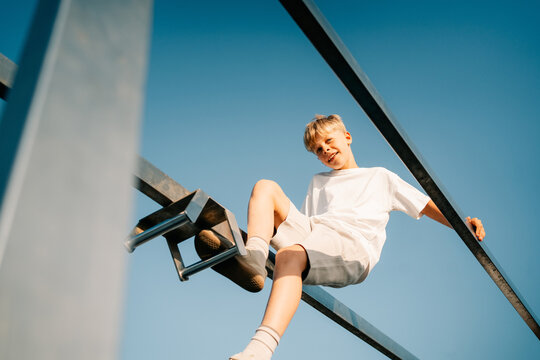 Boy Plays on Metal Structure Under Clear Sky in Daytime