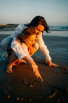 Mother and Child Draw in Sand on Beach During Sunset