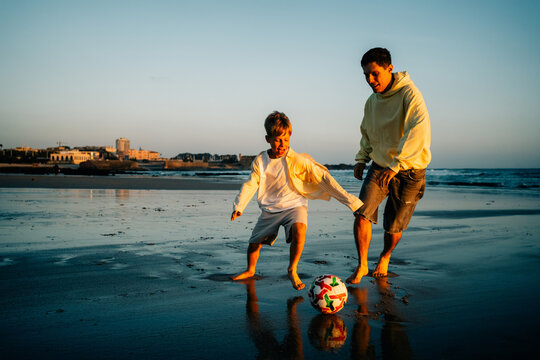 Father and Son Play Soccer on Beach at Sunset