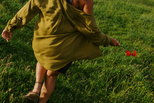 Person walks through green field holding red flower