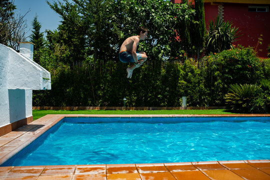 Boy jumping cannonball style into backyard swimming pool