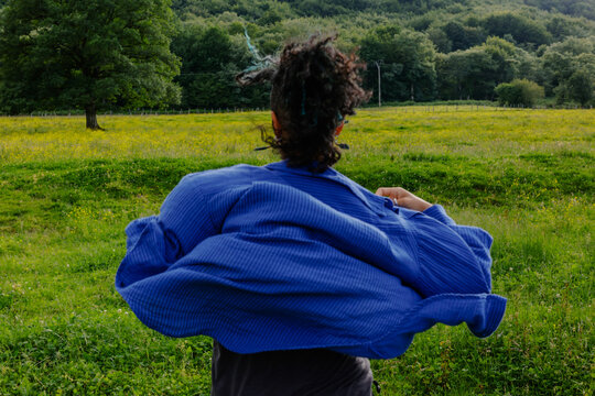 Person spins in a field wearing a blue jacket on a sunny day