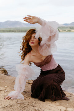 Redhead woman in tulle sleeves posing at lake