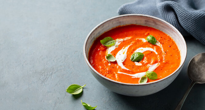 Tomato soup with cream in a bowl on grey stone background. Close up. Copy space.