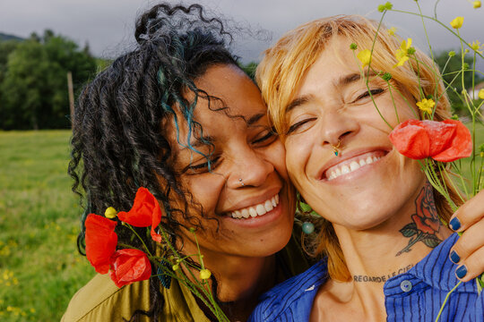 Two friends smile and hold flowers in a green field together