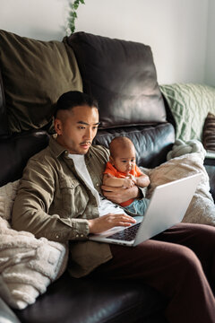 Asian father working remotely with baby at home