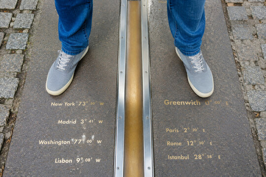 Tourist feet on the brass Prime Meridian line marker outdoors.