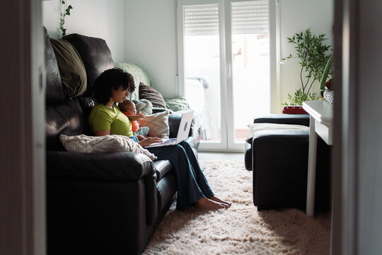 Mother multitasking with baby holding laptop at home