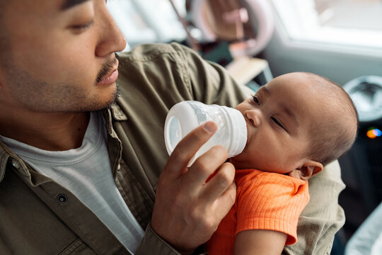 Father feeding multiracial baby bottle at home
