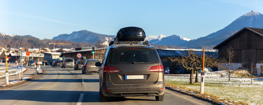 Scenic back view family van car roof box rack luggage drive alpine countryside road cold winter day Europe mountain resort. Automobile vehicle holidays trip journey. Vacation transport seasonal scene