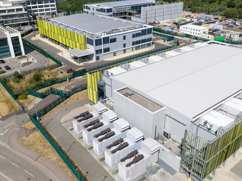 Aerial view of a modern data center facility featuring large industrial buildings, rows of cooling units, and secure perimeter fencing in the United Kingdom.