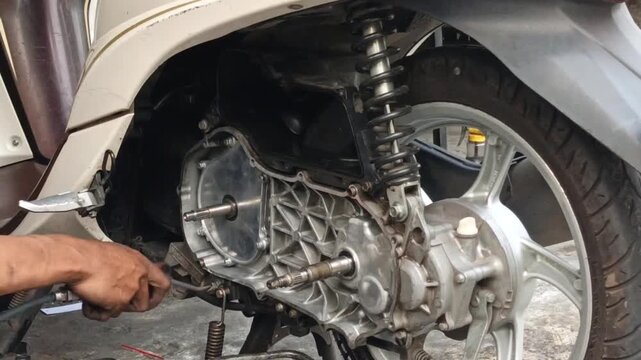 Mechanic uses compressed air to clean a scooter CVT compartment, removing dust and debris during routine motorcycle maintenance in a repair workshop.
