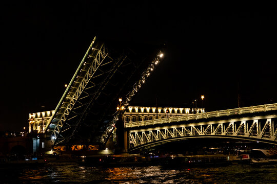 Trinity Bridge in St. Petersburg. Drawbridge in an open position at night, showcasing its intricate structure against the backdrop of illuminated buildings along the river