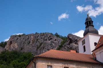 Fototapeta premium Baroque Church of the Nativity of Saint John the Baptist beneath the towering limestone cliffs of Svatý Jan pod Skalou, a historic pilgrimage site in the Bohemian Karst, Czech Republic. 