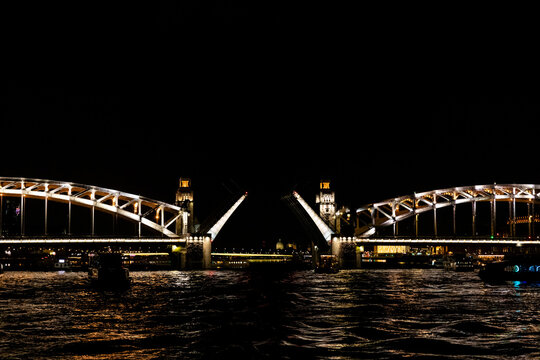 Bolsheokhtinsky Bridge in St. Petersburg. Illuminated drawbridge at night over a river with reflections on the water and city lights in the background, urban landscape. Travel agencies, tour operators
