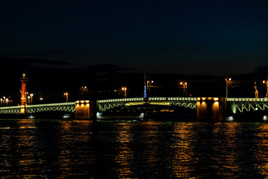 Dvortsovy (Palace) bridge in St. Petersburg. Illuminated bridge spans across water at night, showcasing vibrant city lights and reflections on the surface, picturesque urban landscape