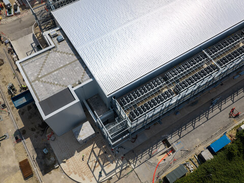 Aerial view of a modern data center facility under construction, featuring a large metallic roof, rows of cooling units, and surrounding paved areas in the United Kingdom.
