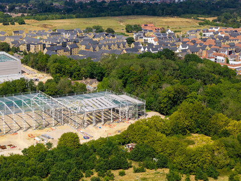 Aerial view of a data center under construction featuring a large steel framework surrounded by lush green trees and a residential neighborhood in the United Kingdom.