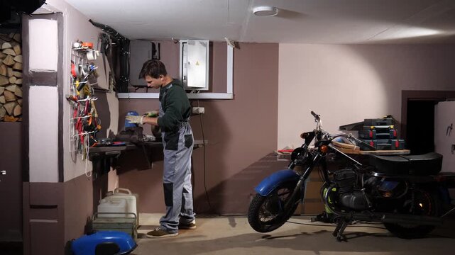 Mechanic working on a motor vehicle engine part with hand tools at a workbench in a home garage, performing maintenance and repair work on a vintage motorcycle