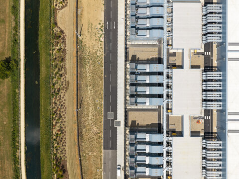Aerial view of Data Center with rows of cooling units and industrial infrastructure adjacent to a road and a canal in United Kingdom.