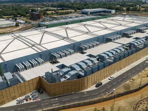Aerial view of a large data center facility with extensive rooftop HVAC cooling units and surrounding infrastructure in the United Kingdom.